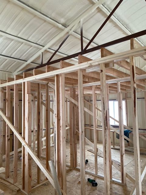 Interior view of a wooden frame structure under construction, with spray foam insulation and a metal roof.