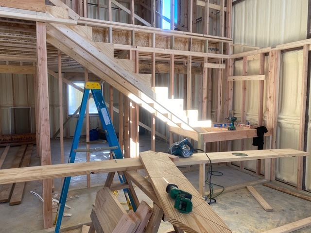 Interior view of a wood-framed staircase under construction, with tools and a blue ladder present.