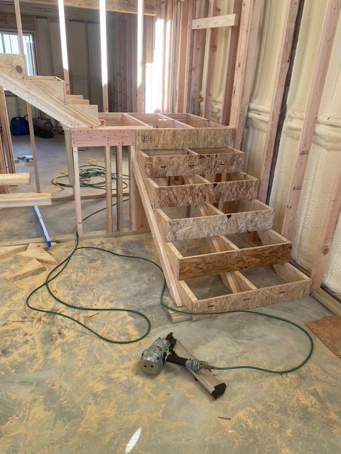 Wooden staircase under construction in a building. Nails gun is on the floor, surrounded by wood shavings.