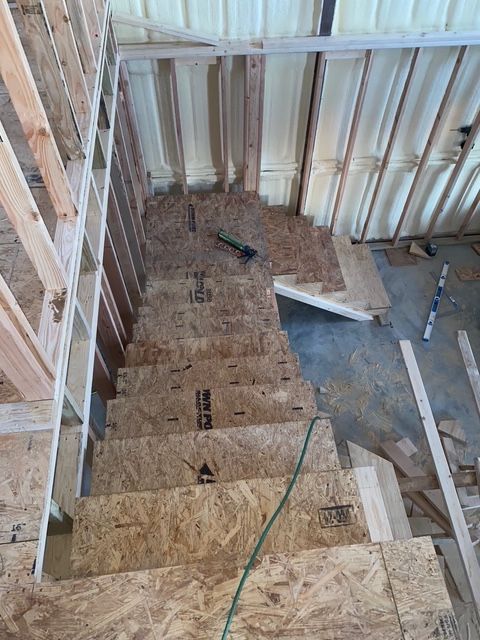 Wooden staircase under construction inside a building. Framing visible; OSB steps.
