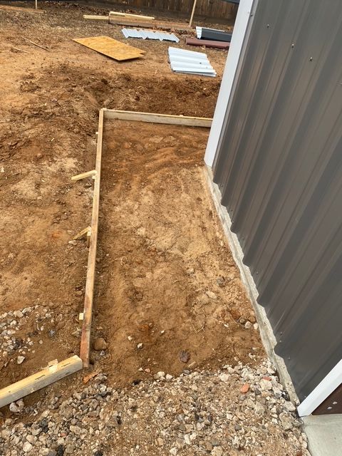 Wooden concrete form next to a building, set in dirt, awaiting concrete pour.