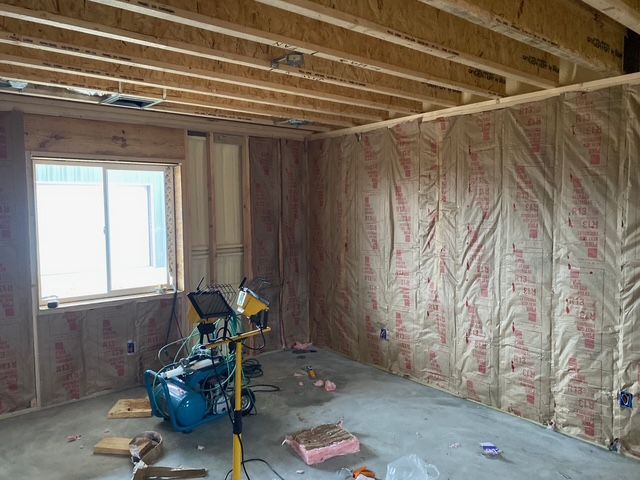 Interior of a room under construction: insulation in walls, unfinished ceiling, window on left, tools on floor.
