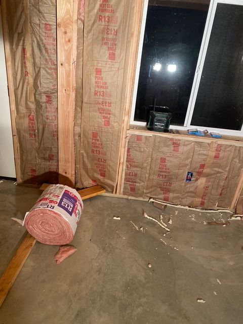 Interior of a room under construction with insulation installed between wood framing; window.