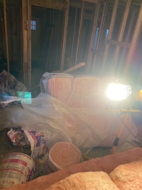 Interior framing and insulation in an attic, illuminated by a work light, showing construction in progress.