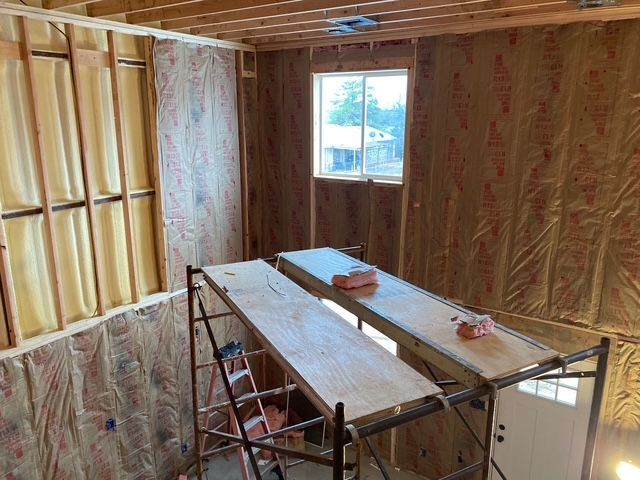 Interior of a room under construction; insulation and window visible; two scaffolds with wooden platforms in the middle.