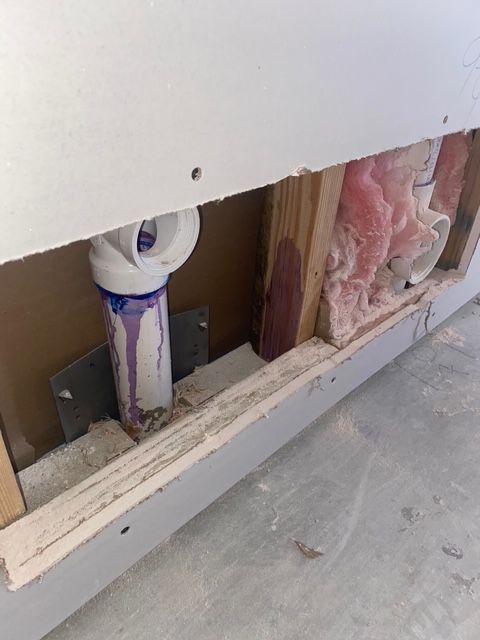Plumbing and insulation exposed within a wall. White PVC pipe with purple primer visible.