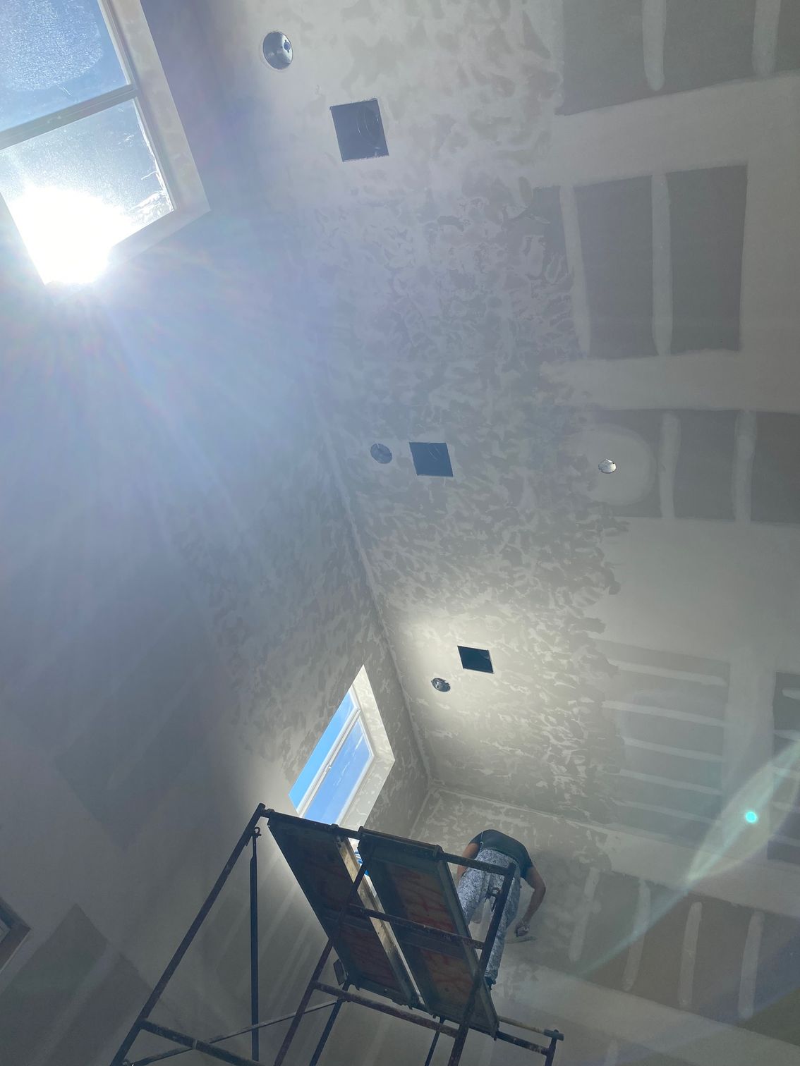 Interior view of a room under construction with unfinished walls and ceiling; sunlight streams through skylights.