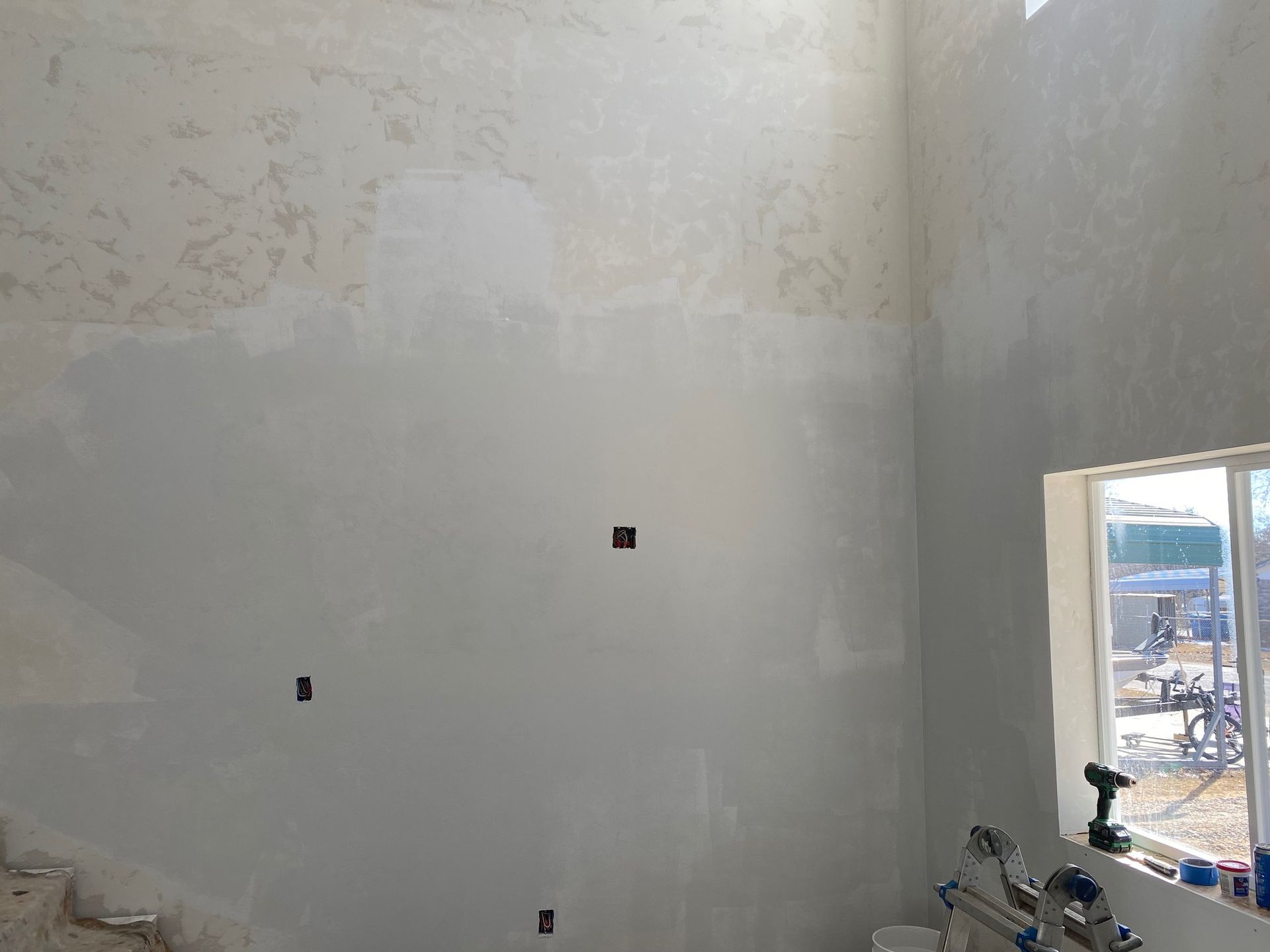 Interior wall with freshly applied drywall, a window, and electrical boxes.