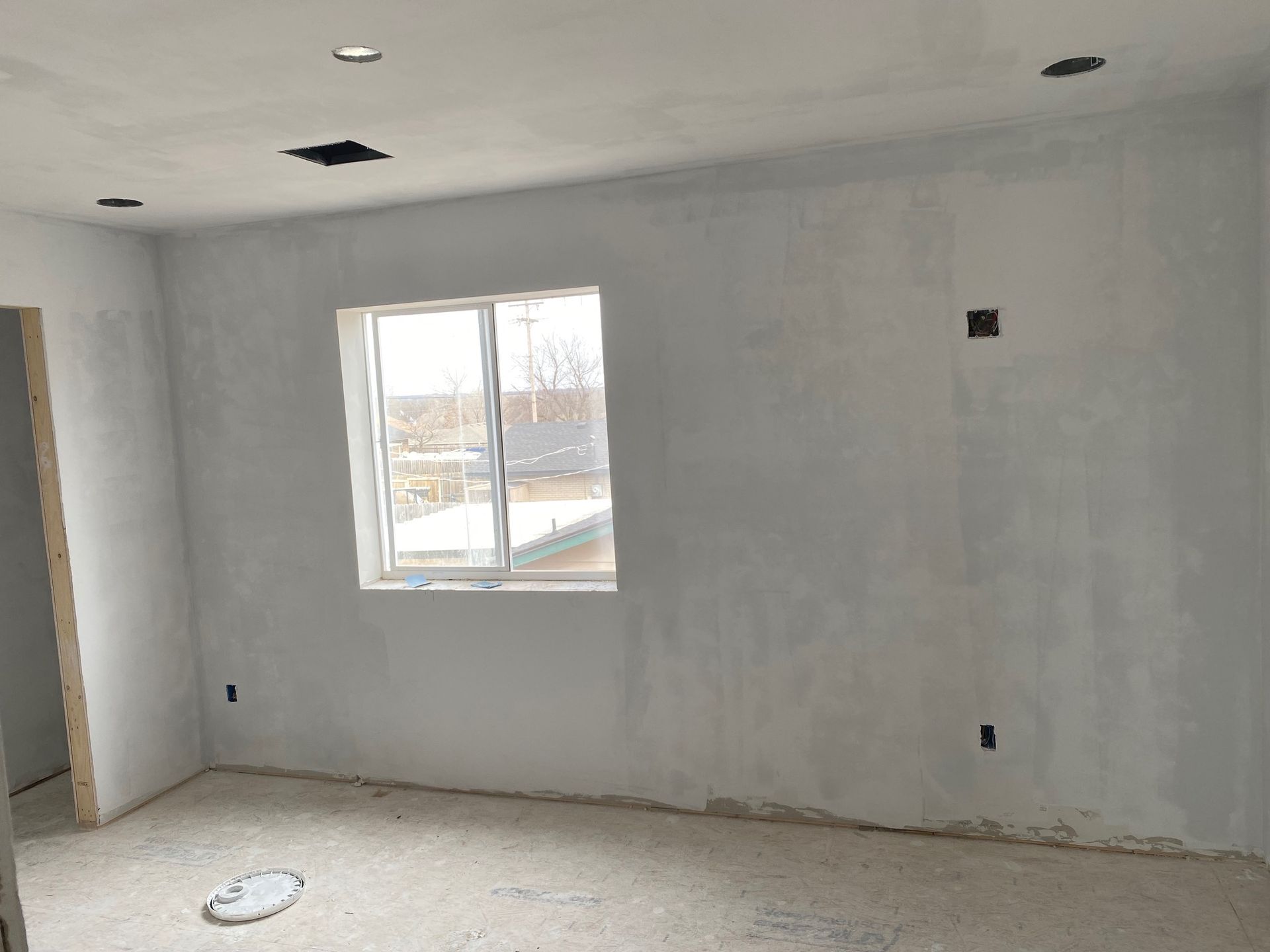 Interior room with unfinished white walls, window, and ceiling fixtures.