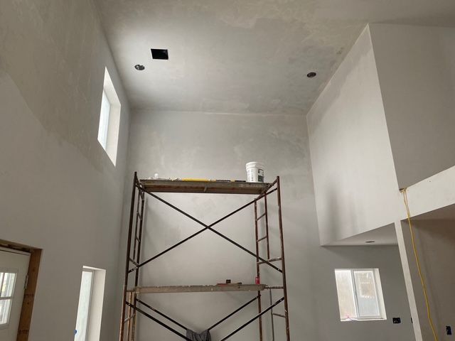 Interior of a room with high ceilings, scaffolding, and partially painted walls in various shades of white.