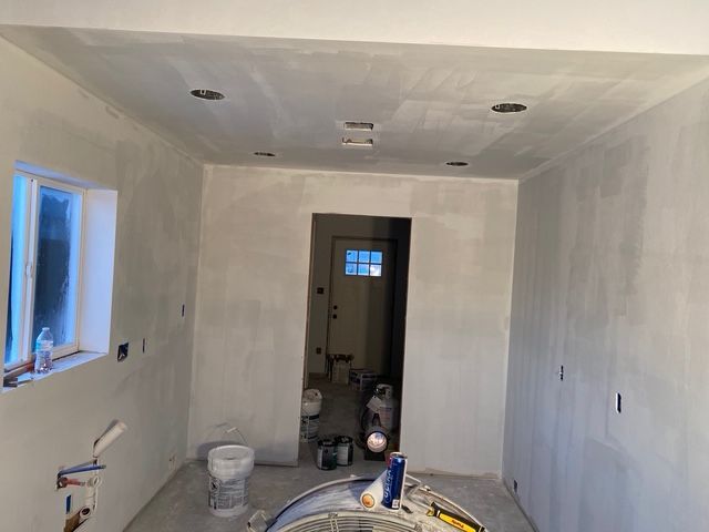 Empty room with white walls, ceiling, and doorway. Recessed lights and small window visible. Construction in progress.