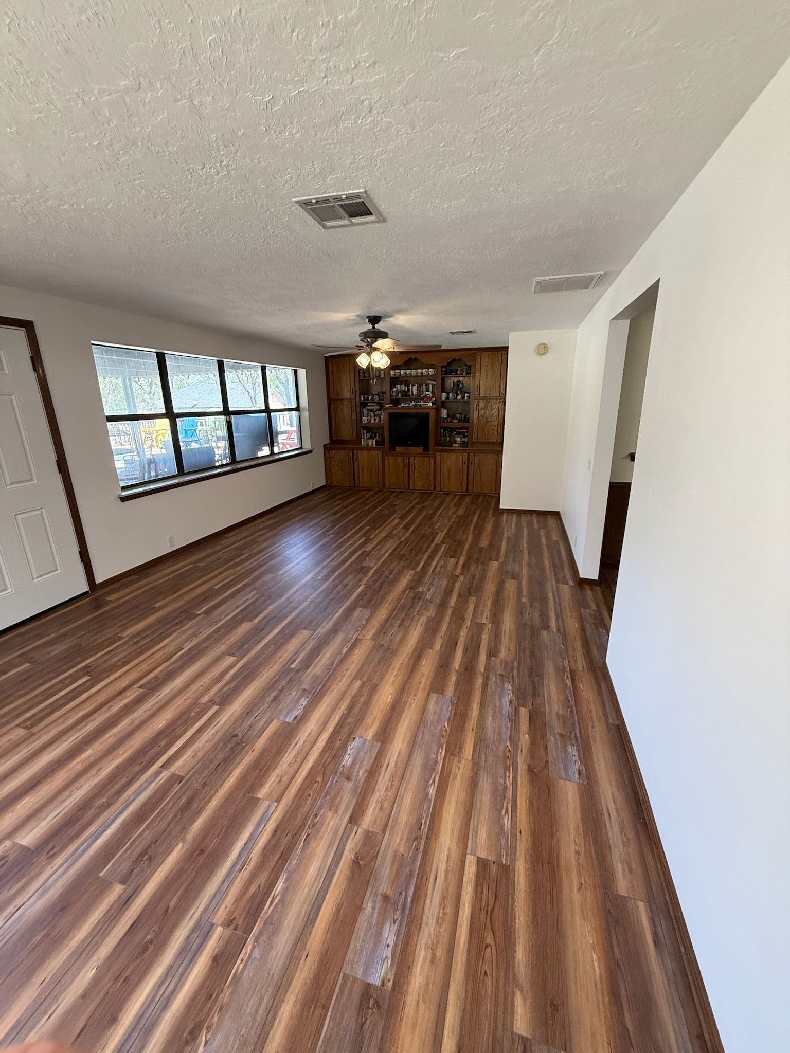Long, empty room with wood-look floor, built-in cabinets, and large windows.