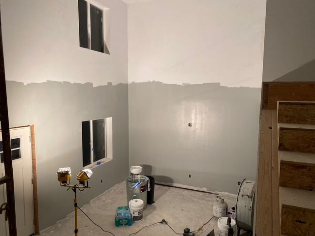 Interior of a room partially painted grey and white, with windows and a construction spotlight.