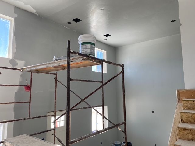 Interior room with scaffolding, fresh gray paint on the walls and ceiling, windows, and a paint bucket.