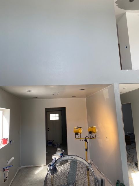 Interior of a room under construction, with white walls, a doorway, and work lights.