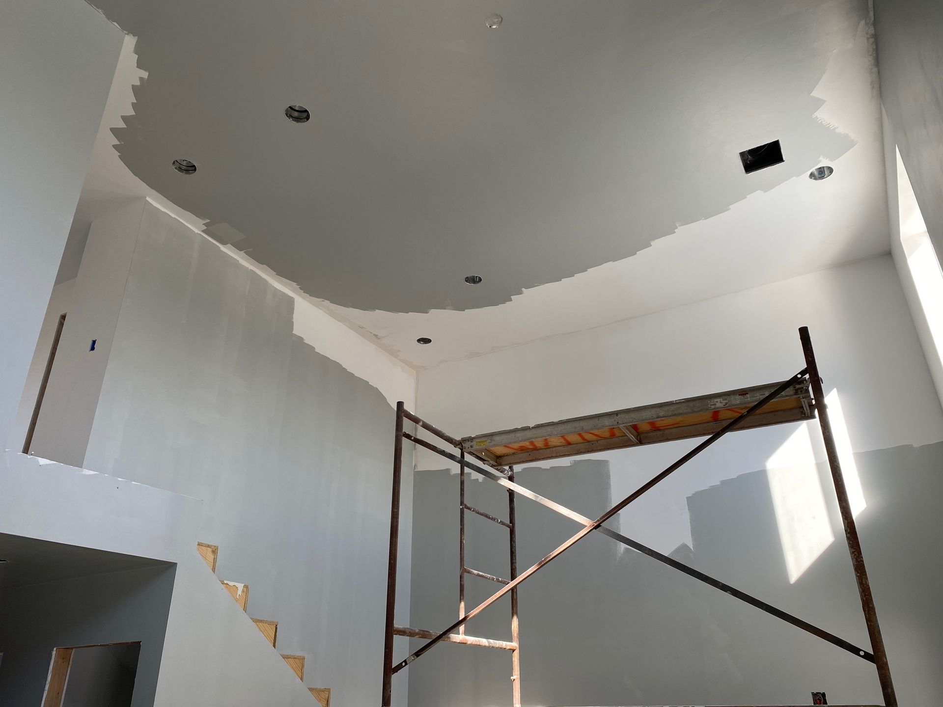 Interior construction: drywall partially painted on ceiling and walls; scaffolding in room.