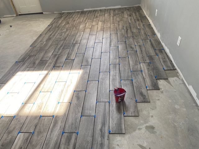 Installing wood-look floor tiles on a concrete surface in a room with gray walls.