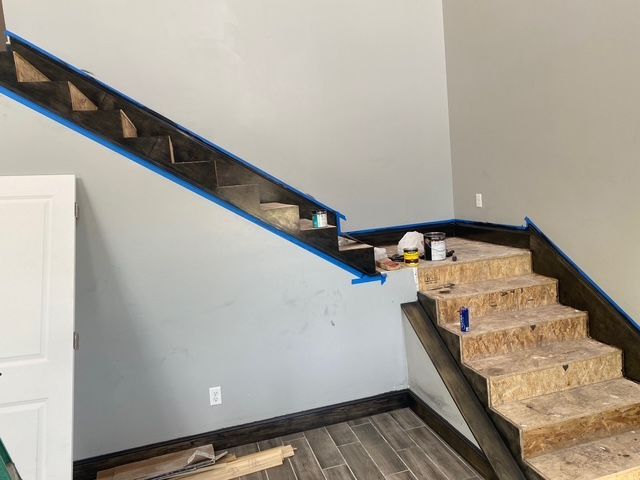 Staircase under construction; wood steps with dark trim and blue painter's tape, interior setting.