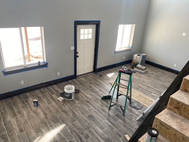Interior room with gray walls, blue trim, gray wood-look tile floor, ladder, and doorway.