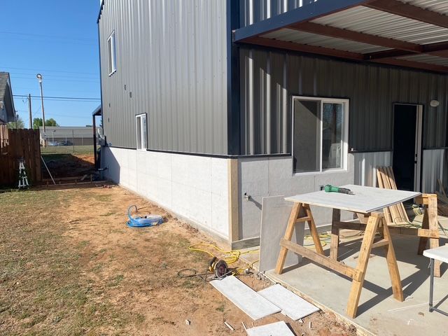 Exterior view of a two-story building with gray siding and a concrete foundation under construction with building materials.
