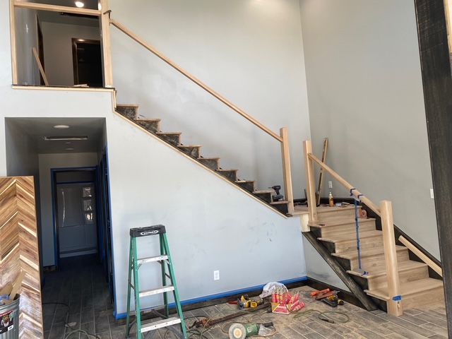 Staircase under construction: light wood steps and railing, gray walls, green ladder, tools on the floor.