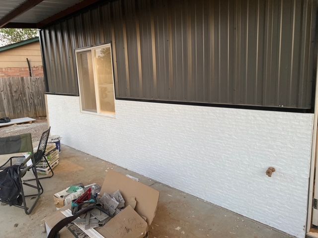 A building with a dark corrugated metal upper section and a white textured lower section, with a window.