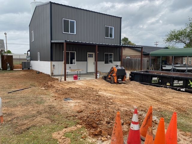 Two-story metal building under construction; orange cones in foreground, dirt and small equipment present.