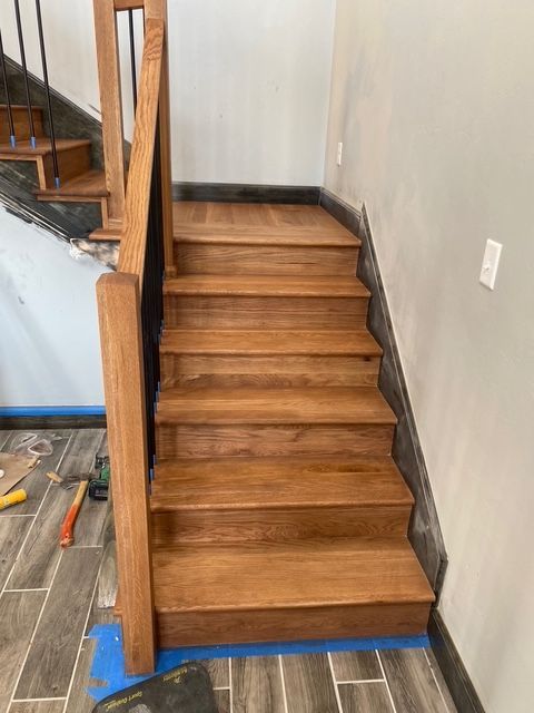 Wooden staircase with a dark railing and light-colored steps against a neutral wall.