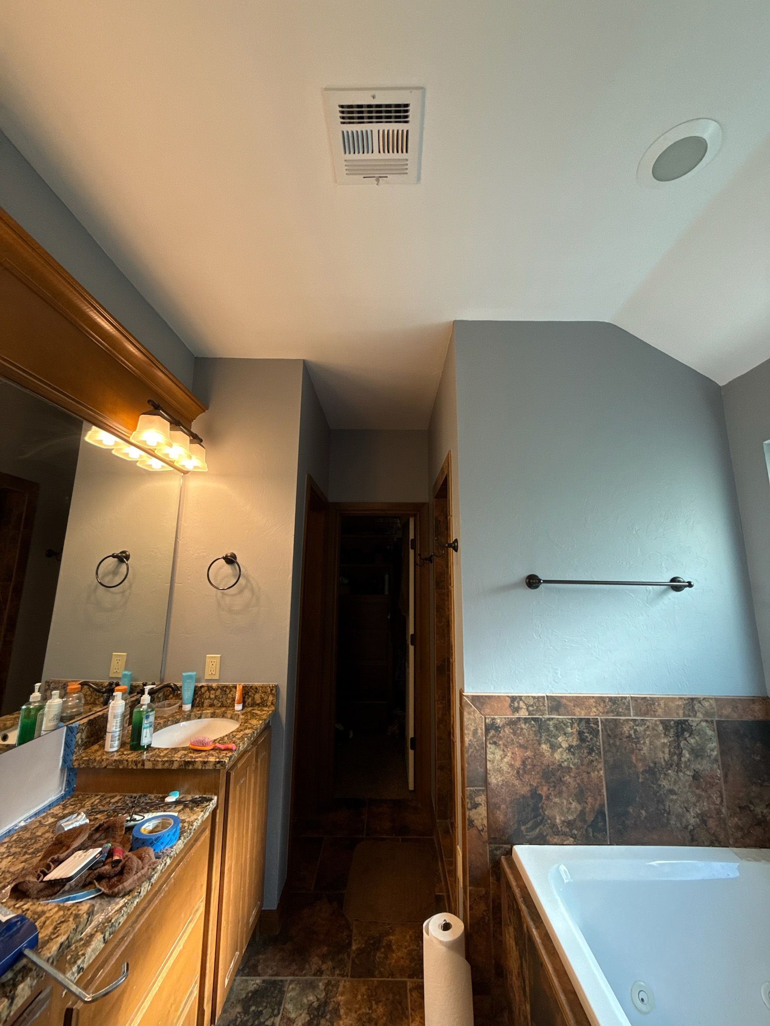 Bathroom with vanity, bathtub, and doorway. Beige countertop and brown tile. Light blue walls.