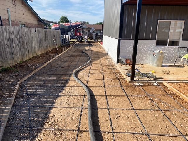 Concrete being poured for a walkway between a building and a fence; a concrete truck is in the background.