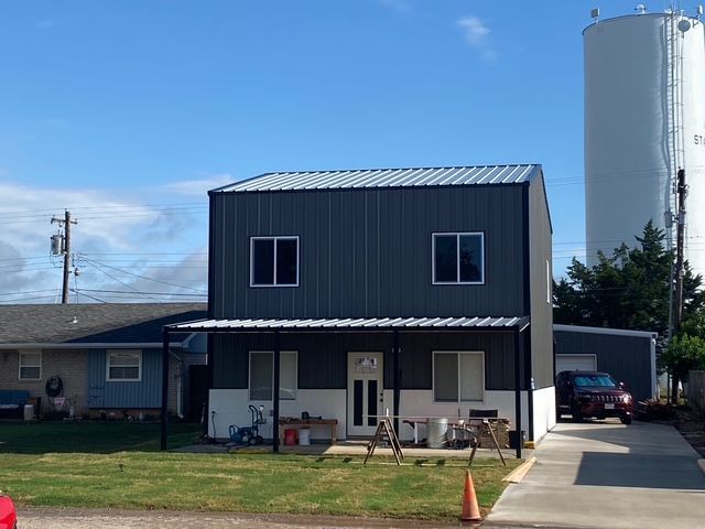 Two-story steel building with a white awning, next to a tall white silo and a parked red car.