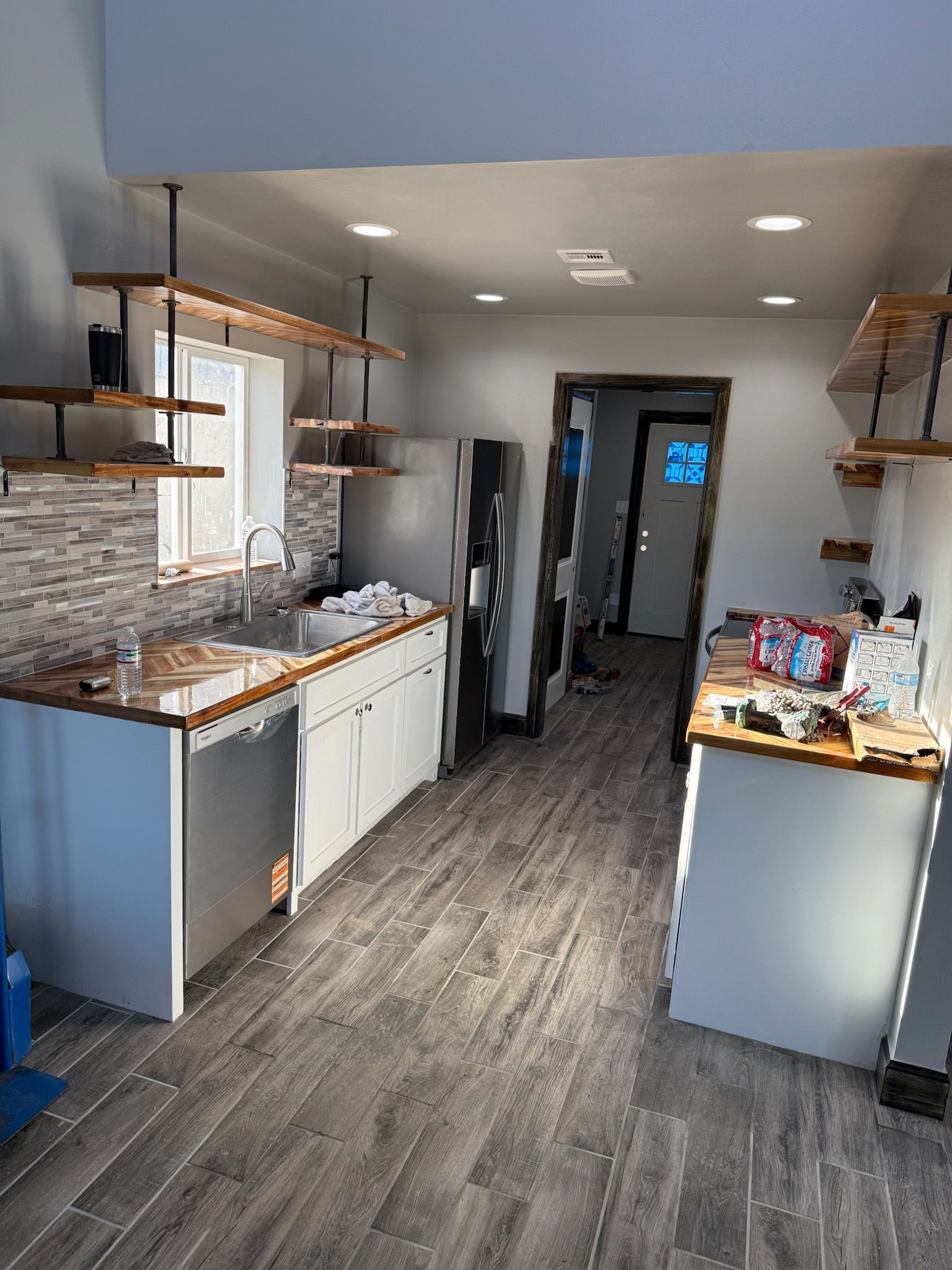 Modern kitchen with white cabinets, wood shelves, stainless steel appliances, and gray flooring.