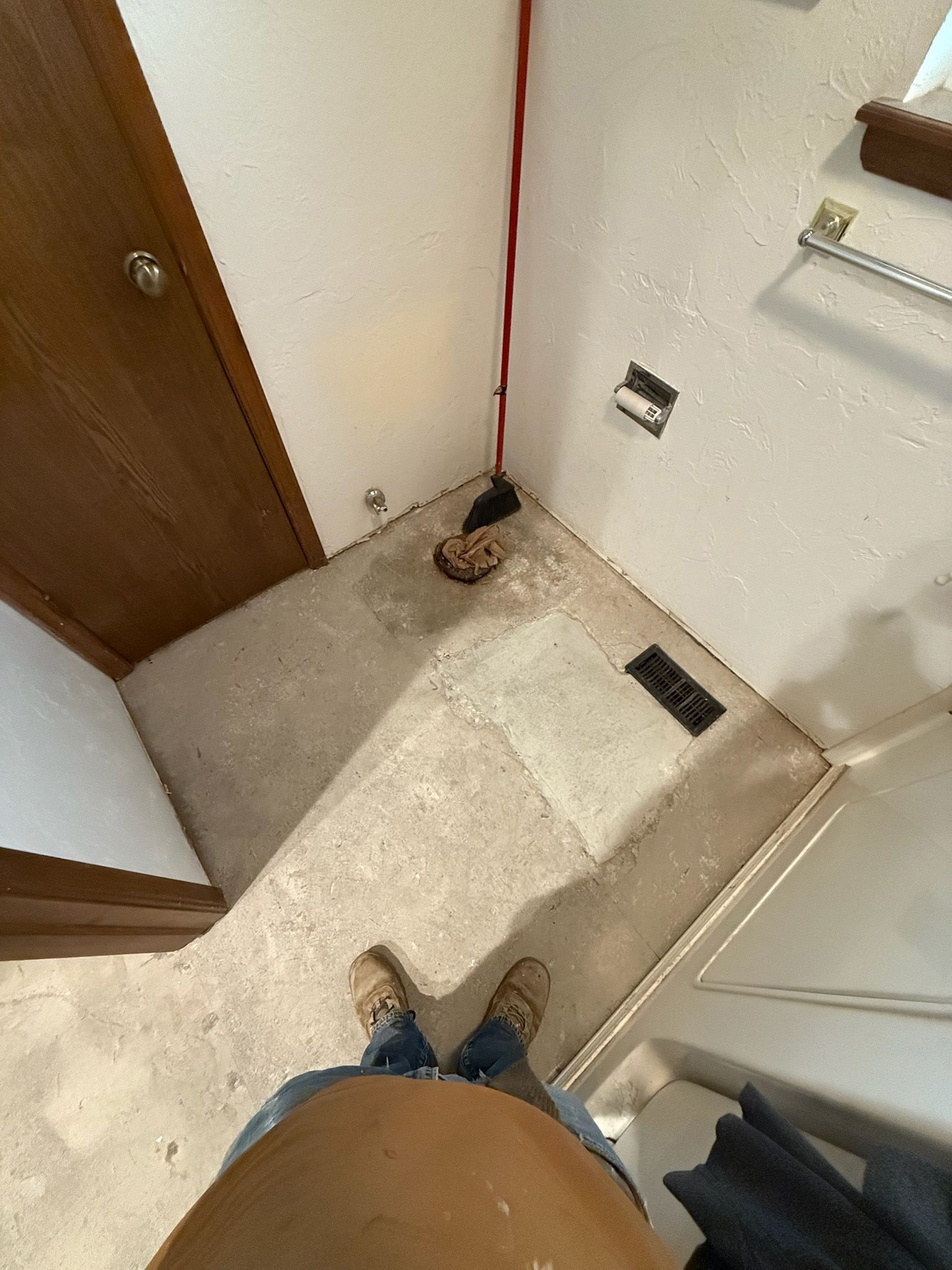 Person standing in a room with concrete floor, bare walls, and a doorway. Electrical wire runs along the wall.
