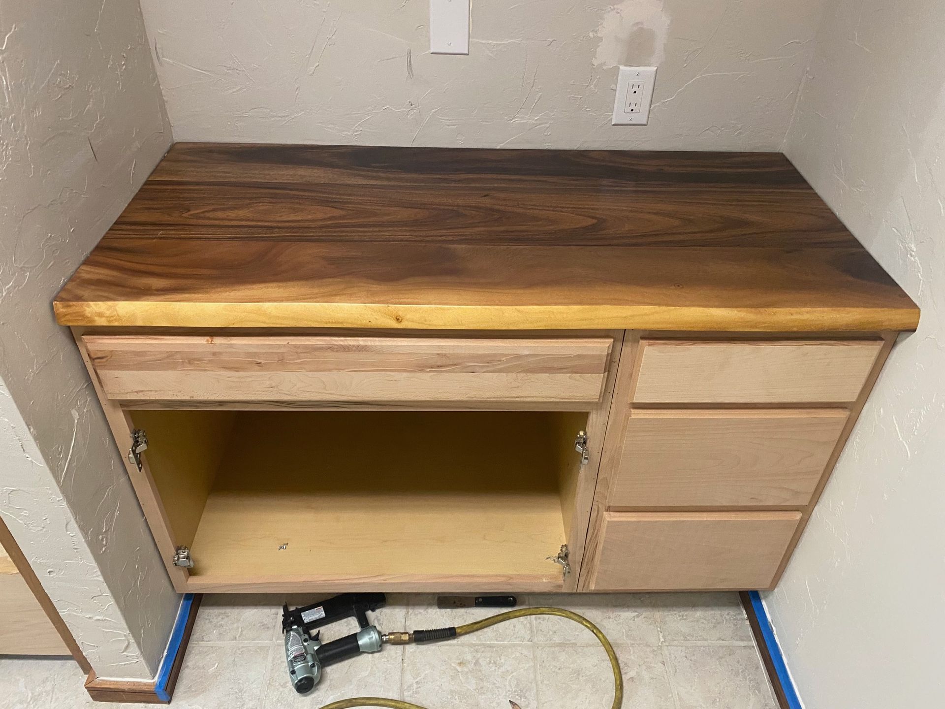 Built-in wooden desk with open cabinet, drawers, and dark wood countertop in a room.