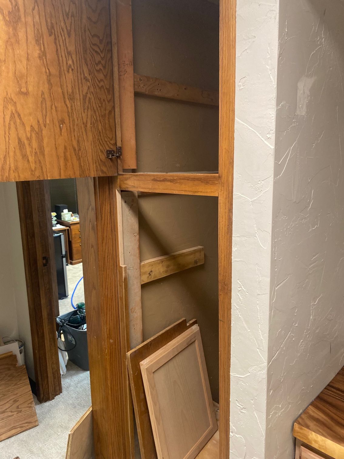 Open wooden cabinet with removed doors, against a textured beige wall.