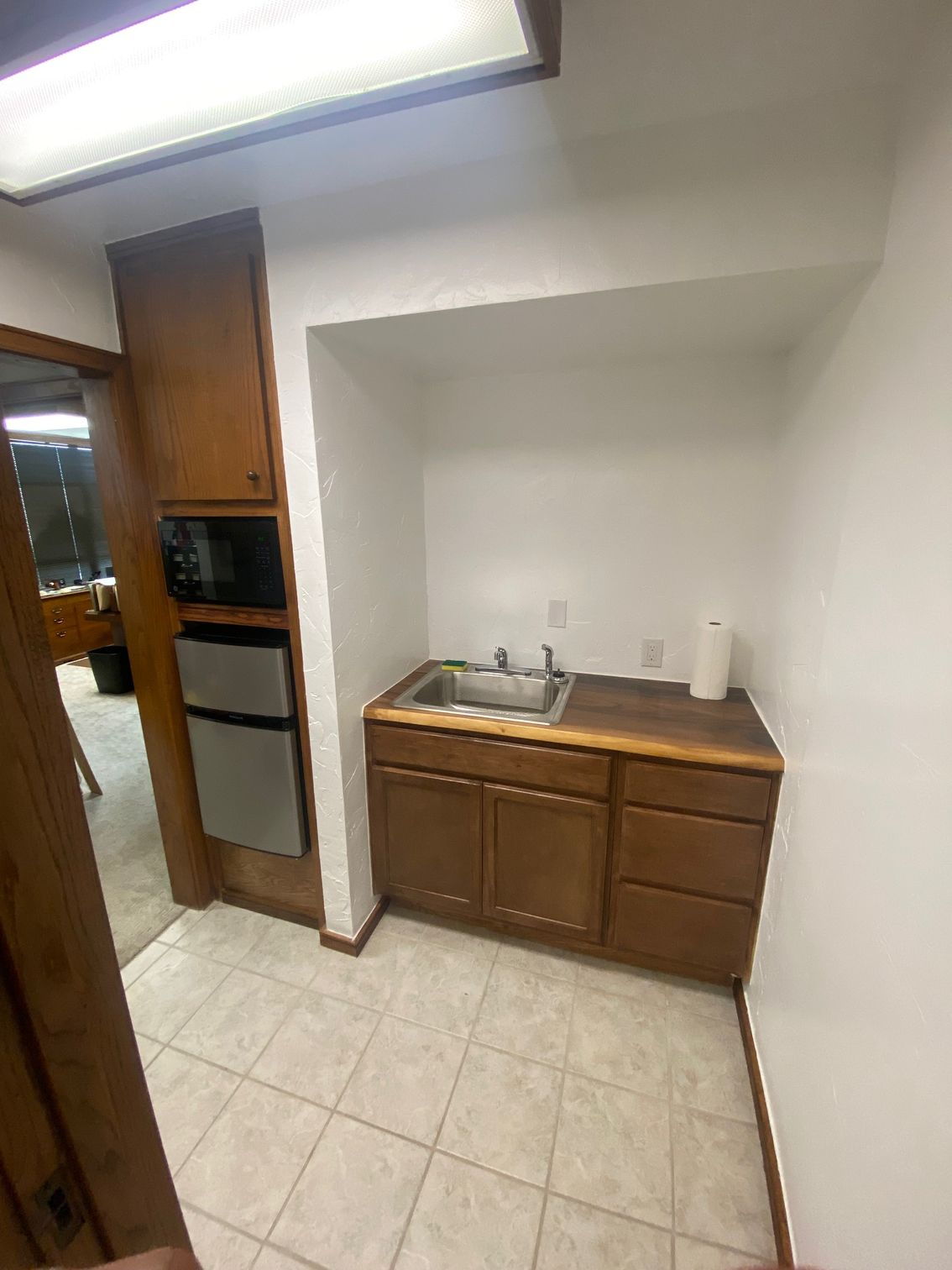 Small office kitchenette with sink, cabinets, microwave, and mini fridge.