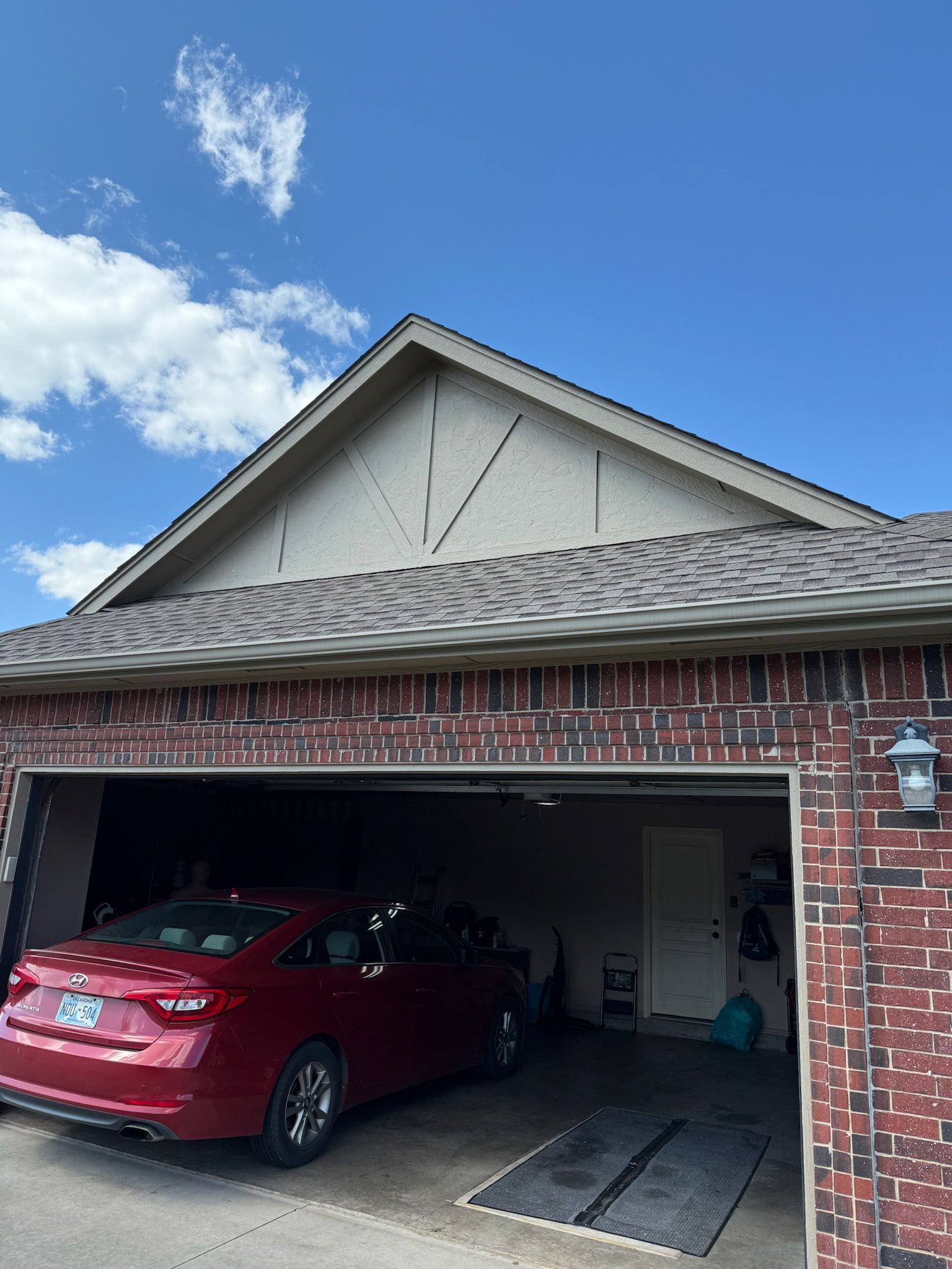 Red car parked in garage under a brown brick exterior with a blue sky background.