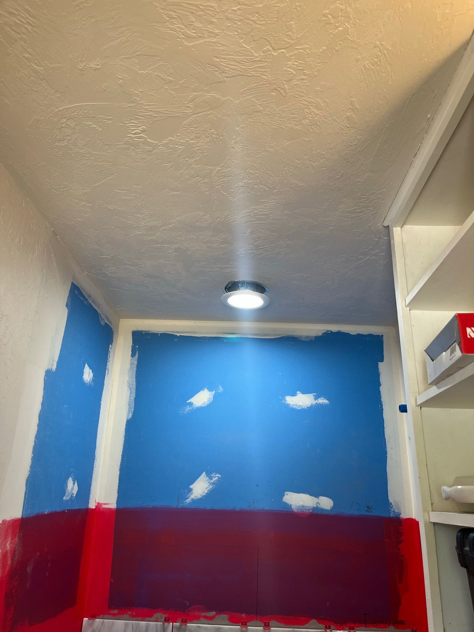Closet ceiling with recessed light. Blue and red painted walls. White shelves on right.