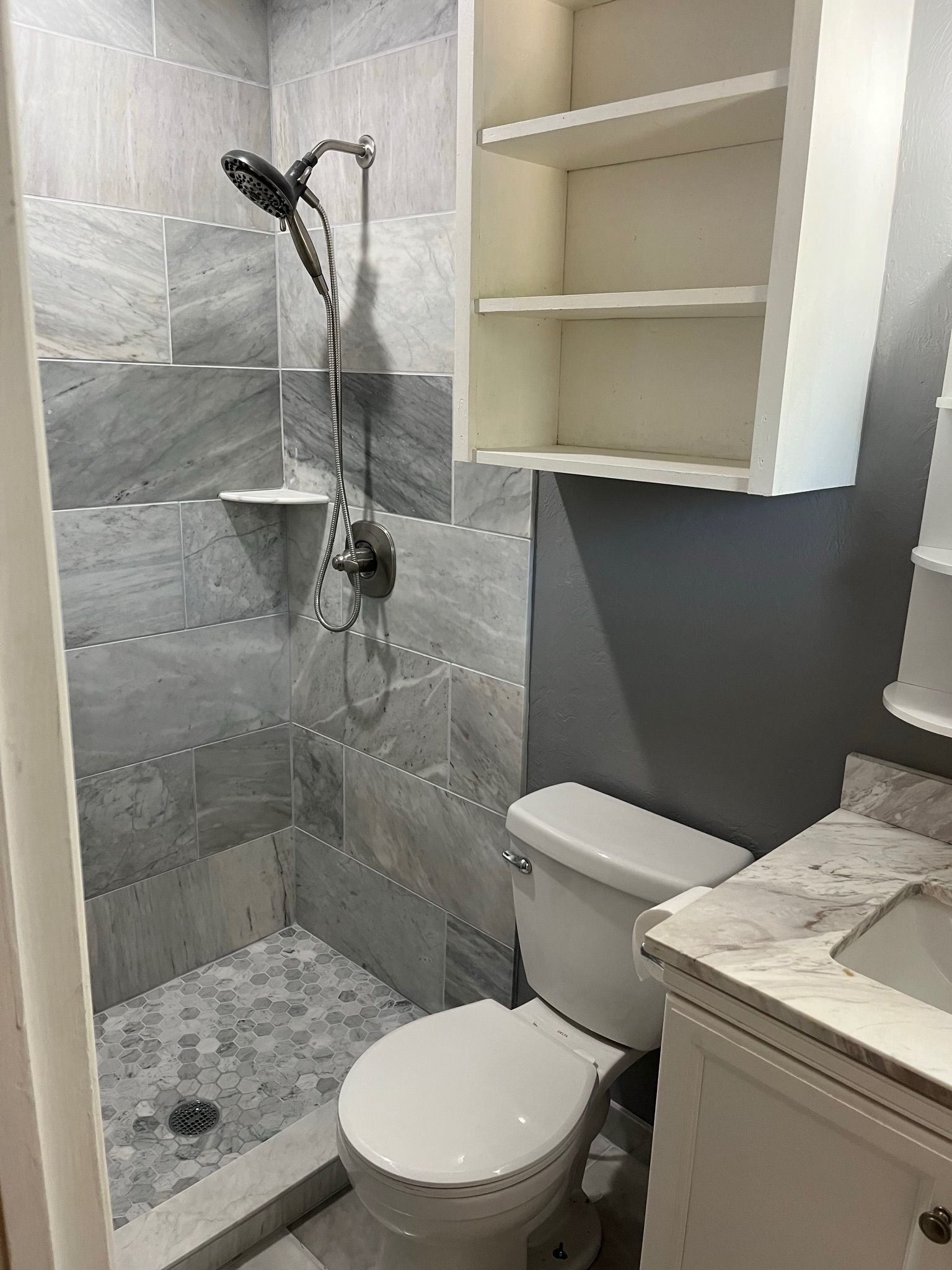 Bathroom with grey tile shower, white toilet, and vanity.