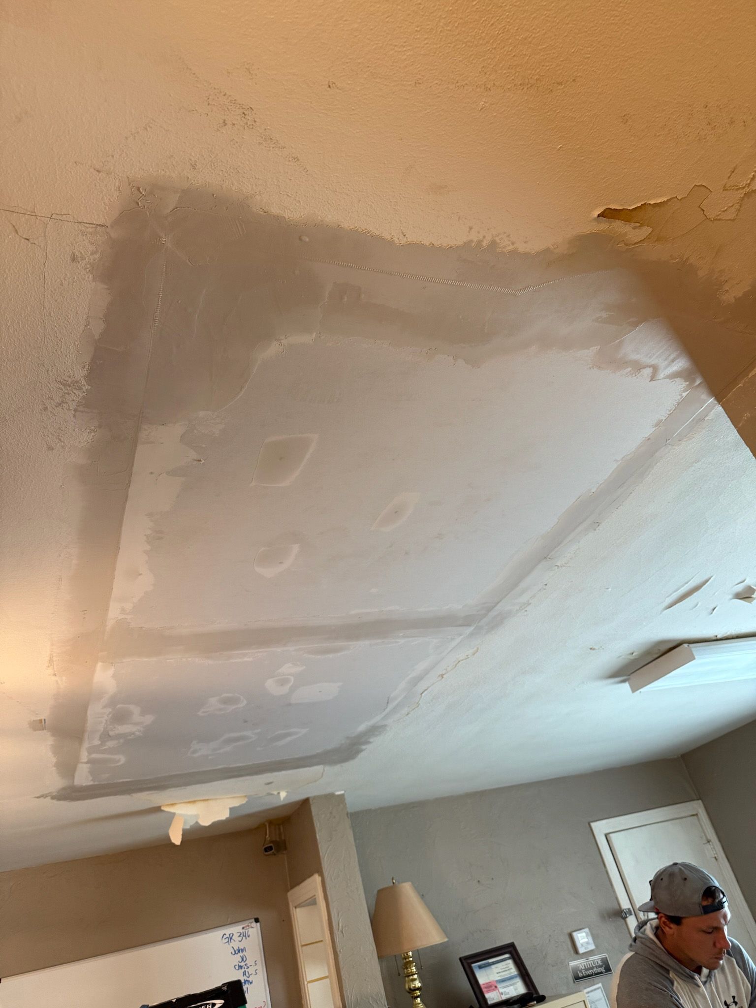 Ceiling with large areas of peeled paint and repaired plaster; a person in a cap is in the room.