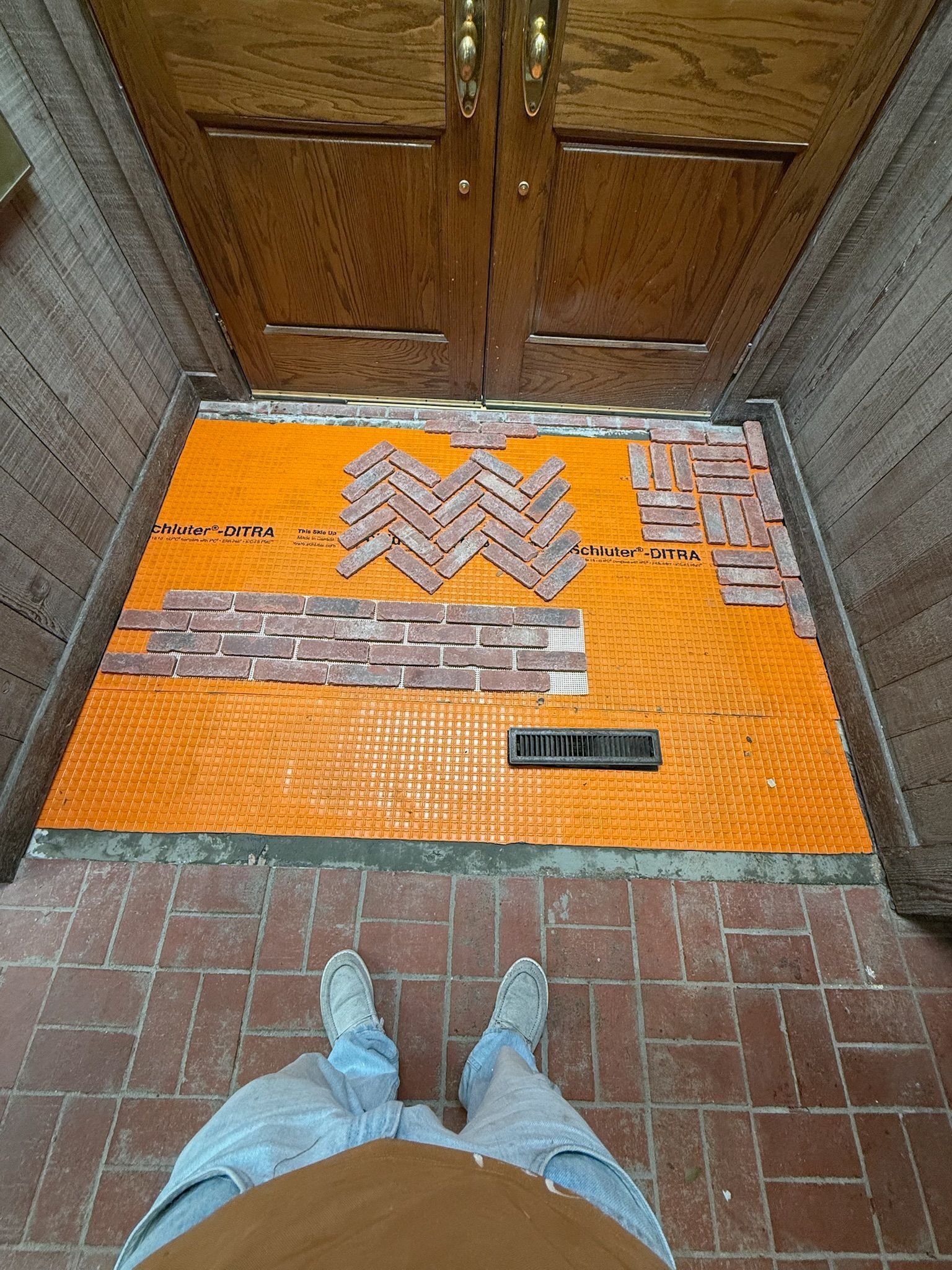 Person standing in doorway with unfinished brick and tile floor work in progress.
