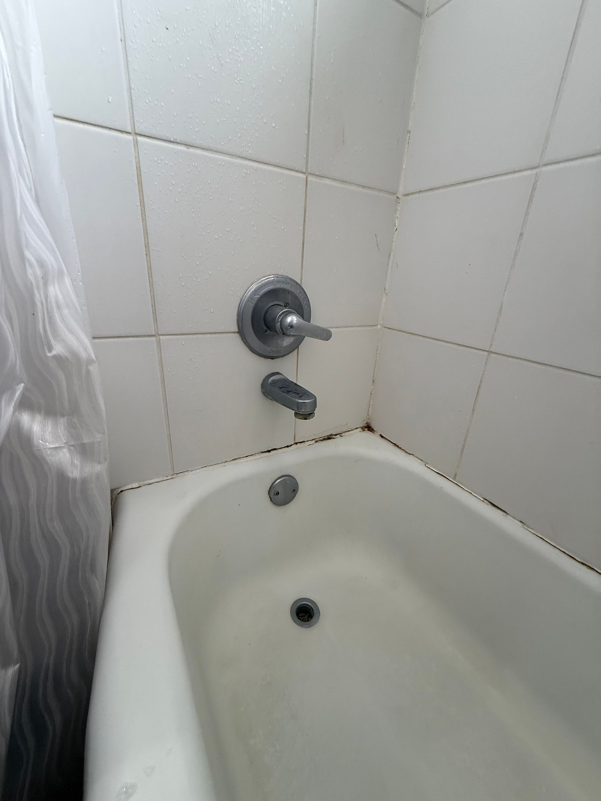 White bathtub with faucet and showerhead, surrounded by white tiled walls, and a white curtain.