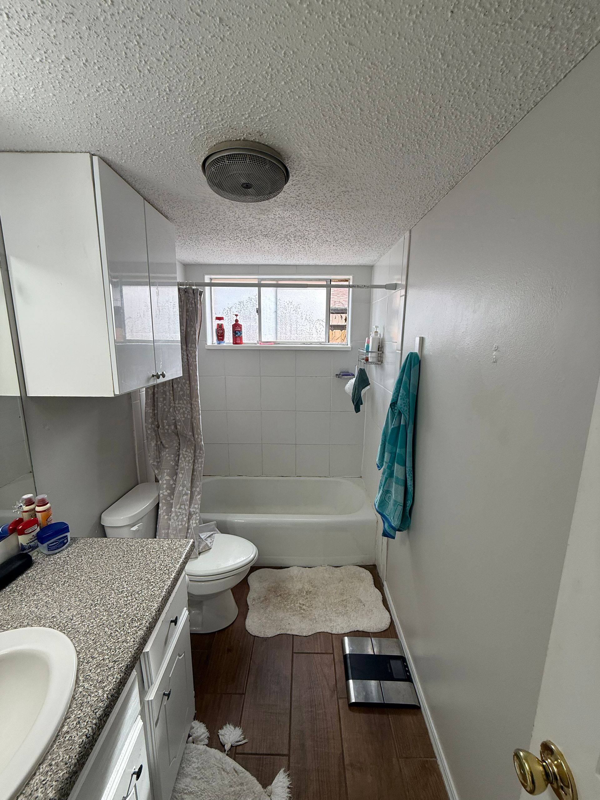 Small bathroom with white walls, a tub, toilet, and vanity with granite top.
