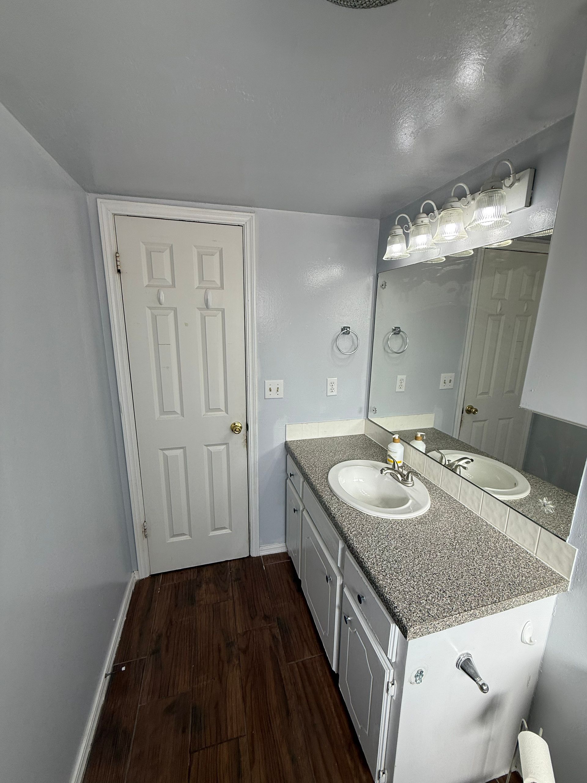 Bathroom with a white door, a white vanity with a granite countertop, and a large mirror.