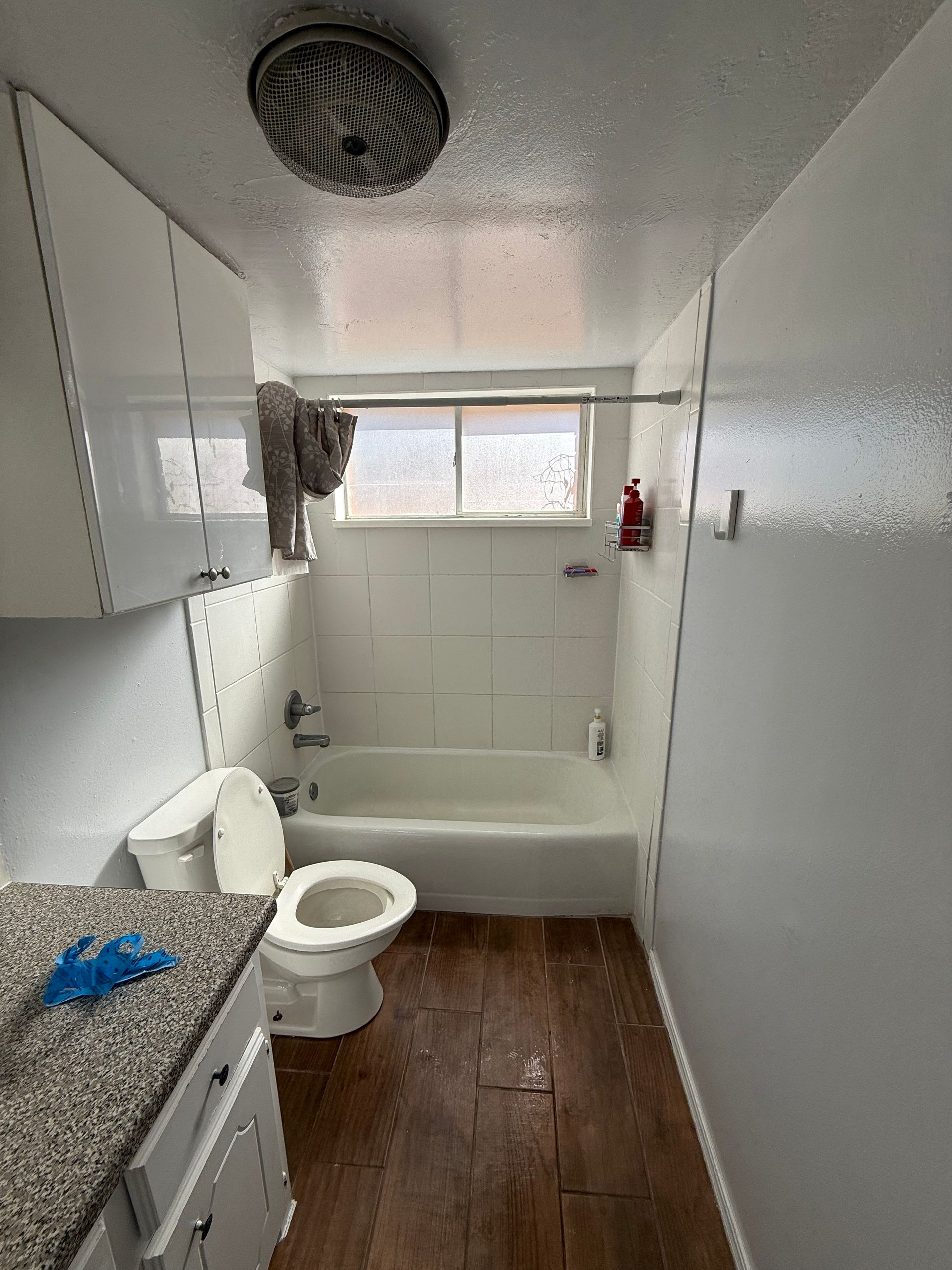 Small bathroom with white fixtures, brown floor, and small window.