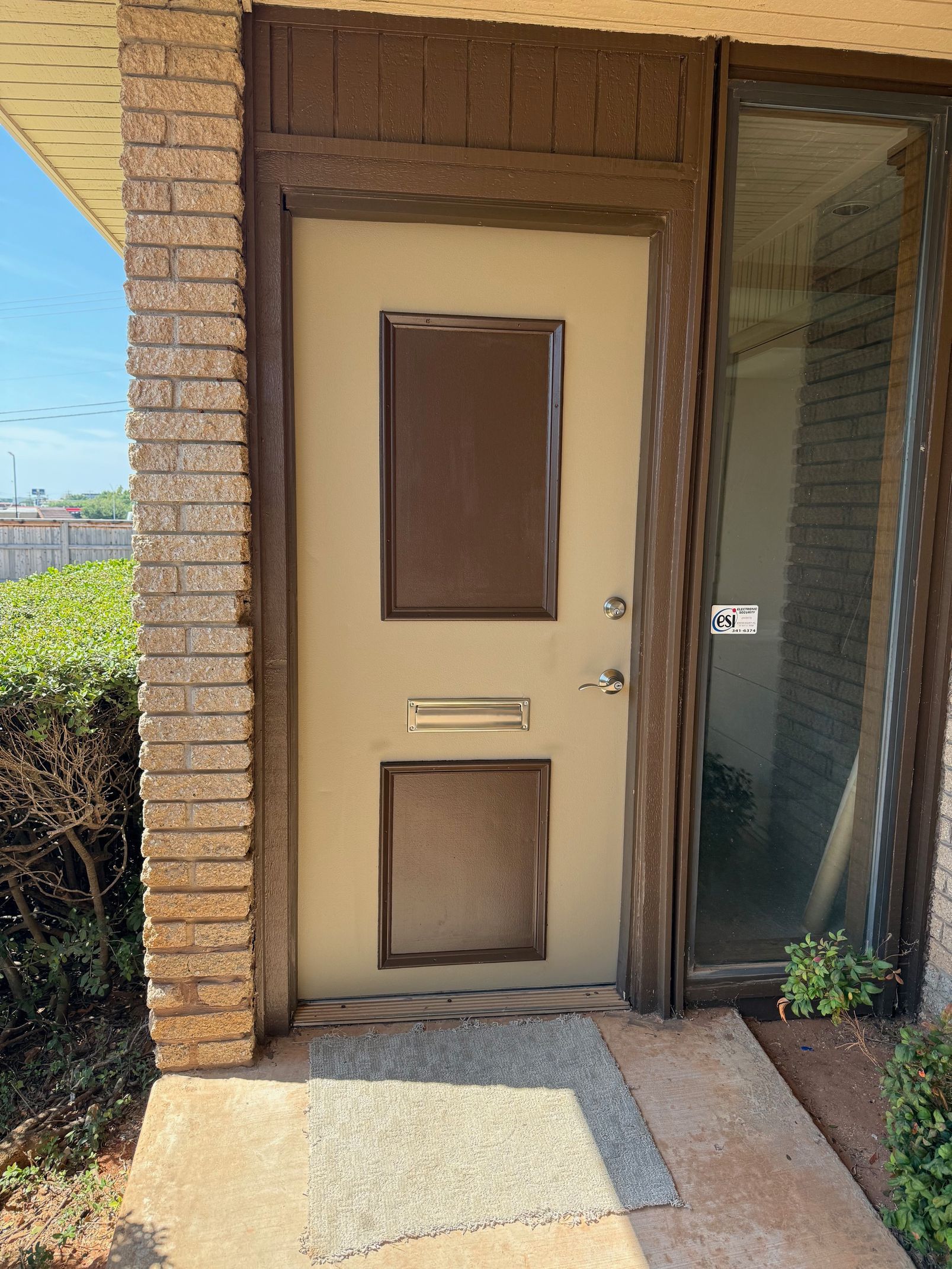 Beige front door with rectangular windows and a doggy door, framed by brick and wood trim.