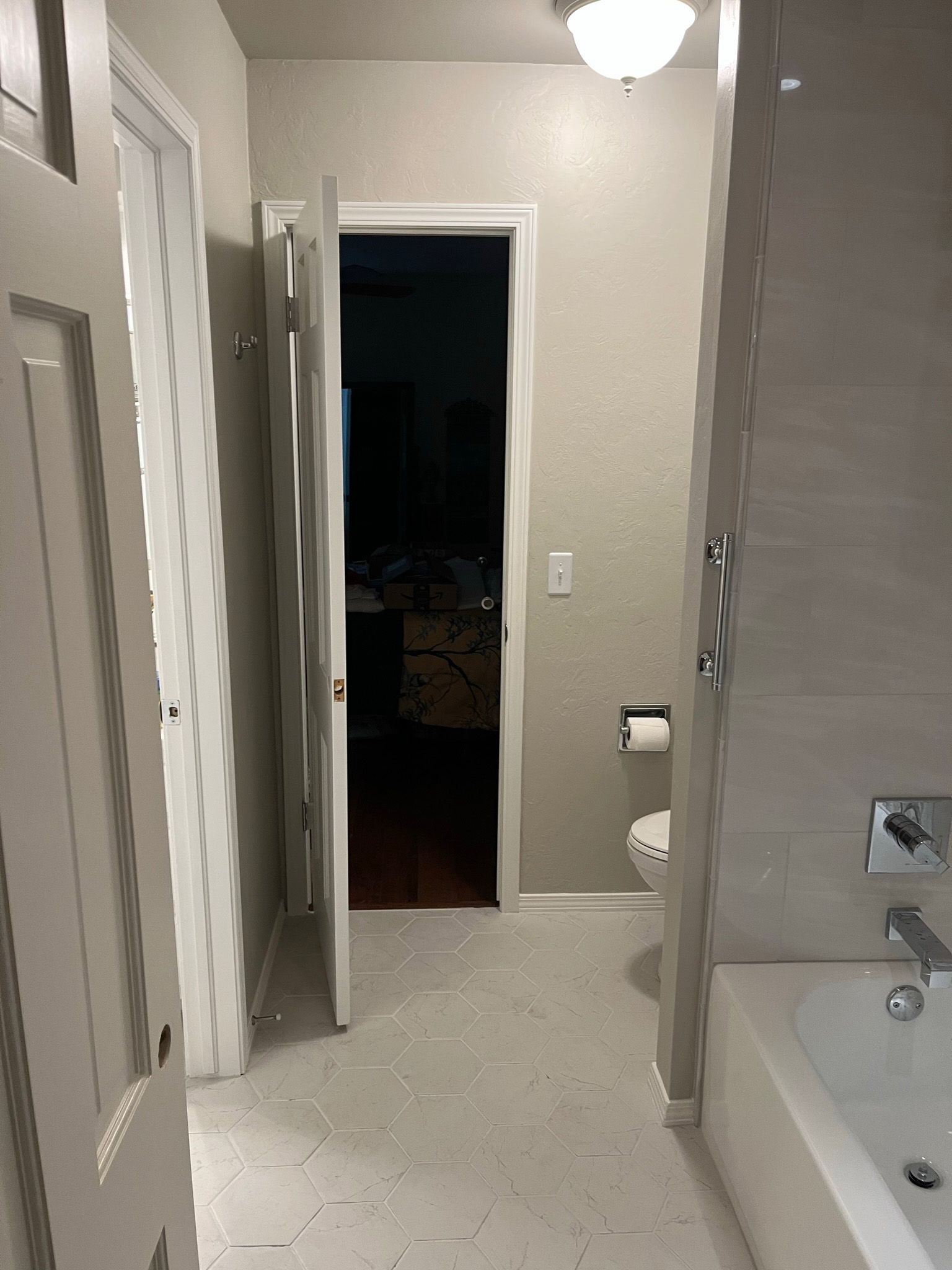 Bathroom with an open door, toilet, bathtub, and gray tile floor.