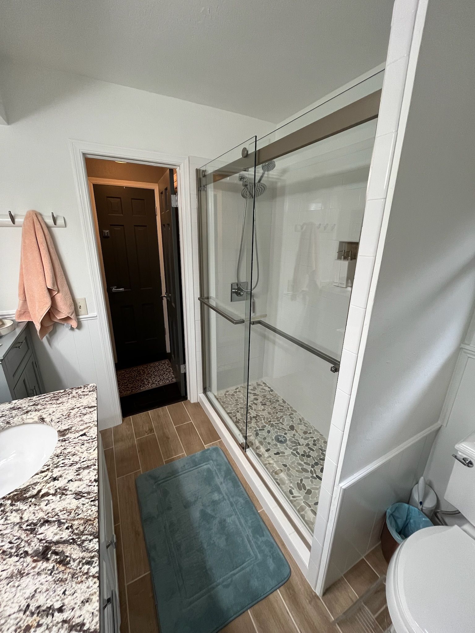 Bathroom with a shower, toilet, vanity, and open doorway with a dark door.