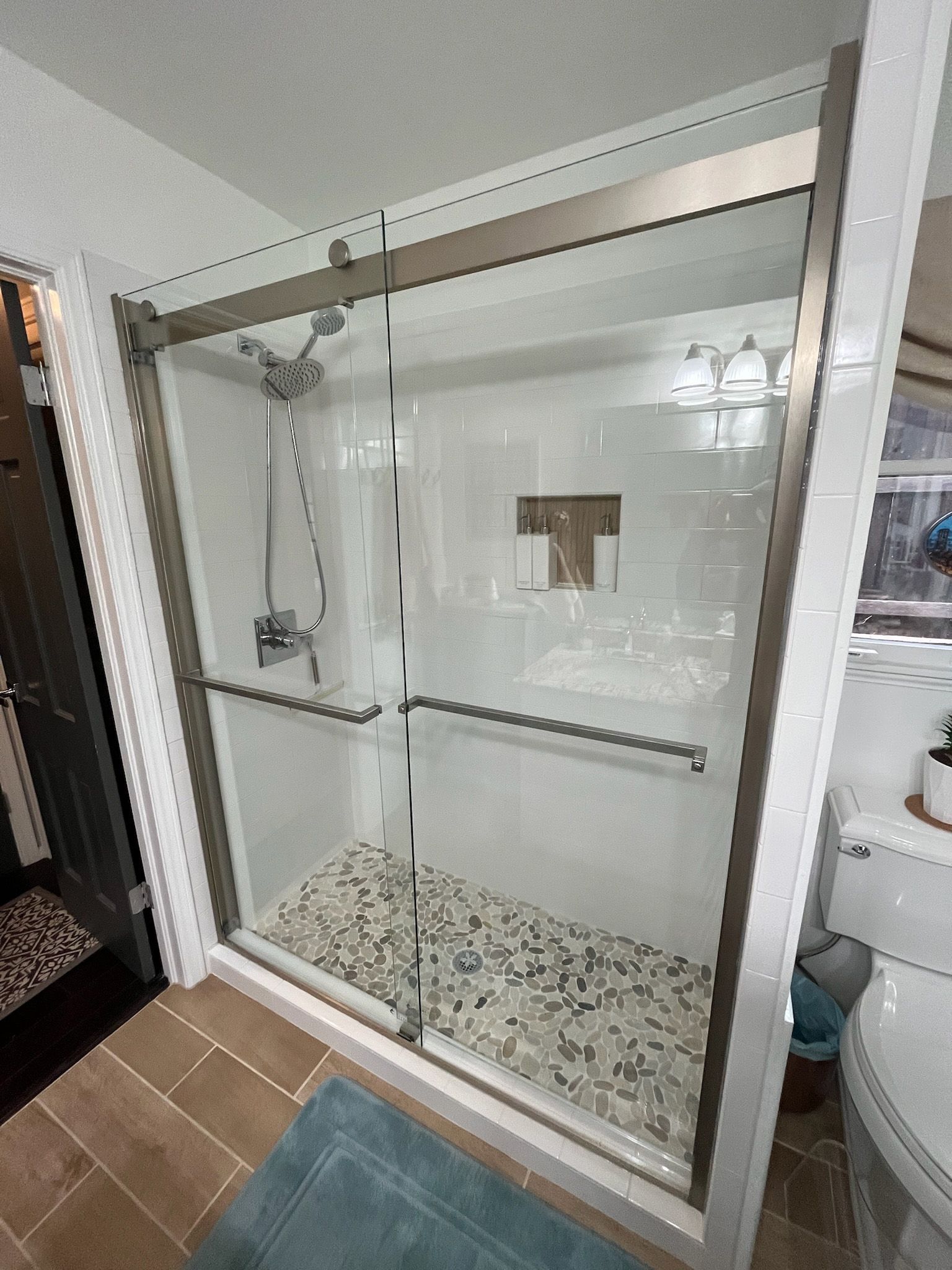 Shower with glass doors and stone tile floor. Chrome fixtures.