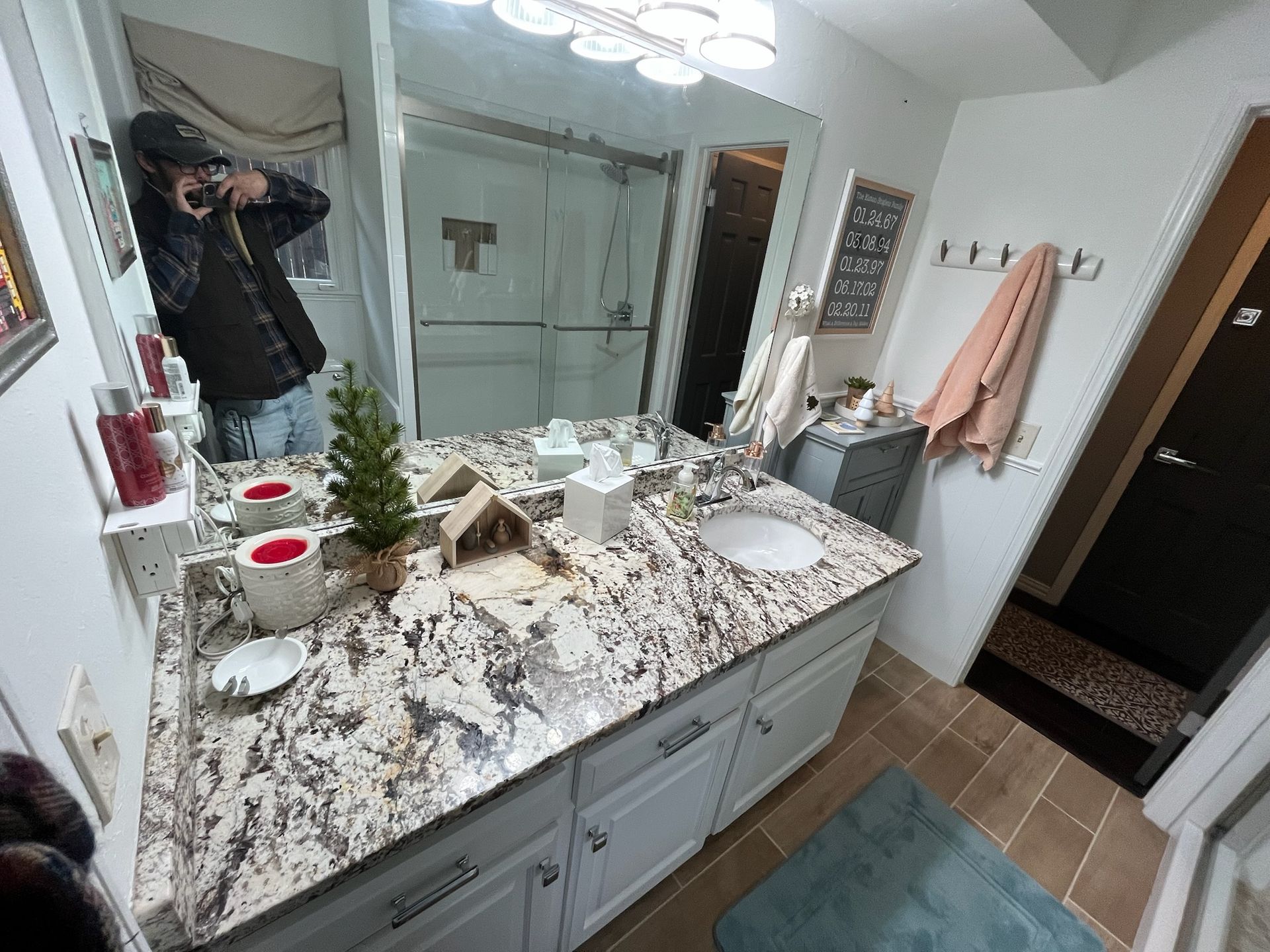 Bathroom with granite countertop, double sinks, mirror, and a person taking a photo.